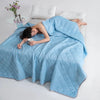 Woman lying on a bed under a blue quilt holding a mug.