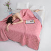 Woman lying on a bed under a pink quilt with a tablet on her chest, in a bedroom setting.