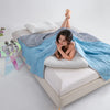 Woman lying on a bed under a blue and gray weighted blanket with a white pillow and minimal decor.