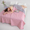 Woman lying on a bed under a pink and gray quilt with a small pillow and flowers in the background.