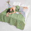 Person lying on a bed under a green quilt with a book and blanket on a white background