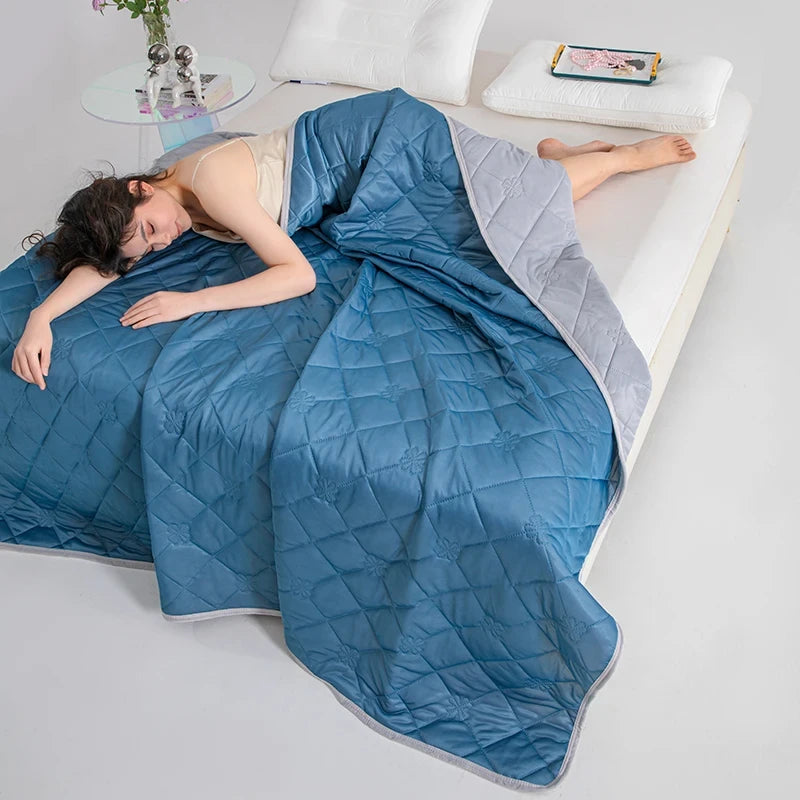 Person lying on a bed under a blue weighted blanket with a white pillow and small table in the background.