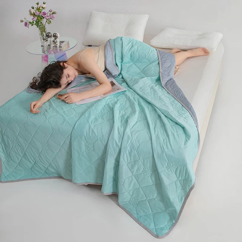 Woman lying on a bed under a light blue quilt with a gray border, reading a book.